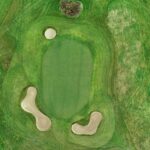 A stunning aerial view of a green at Galway Bay Golf, surrounded by three strategically placed sand bunkers that add challenge and visual appeal. The well-manicured putting surface is seamlessly integrated into the surrounding fairway, with natural rough and undulating terrain enhancing the beauty of the hole. The layout offers a picturesque and demanding approach for golfers.
