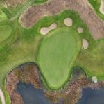 A stunning aerial view of a green at Galway Bay Golf, surrounded by multiple sand bunkers and bordered by a natural water hazard. The green’s smooth contours contrast beautifully with the rugged terrain, blending seamlessly into the surrounding fairway. The combination of strategic bunkering and the nearby marshland adds both challenge and scenic beauty to this coastal golf hole.